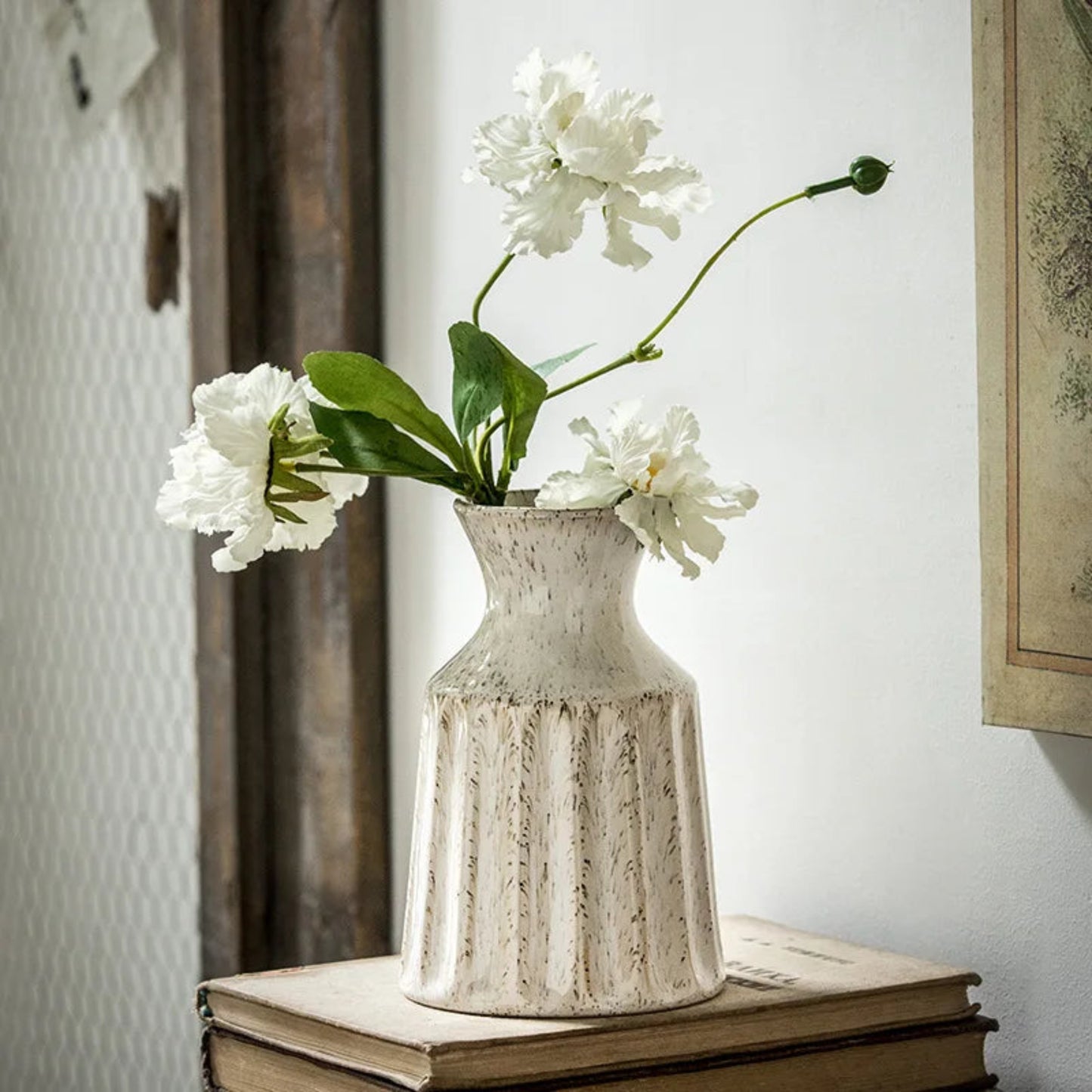 White flowers in a textured vase on top of books with a neutral background