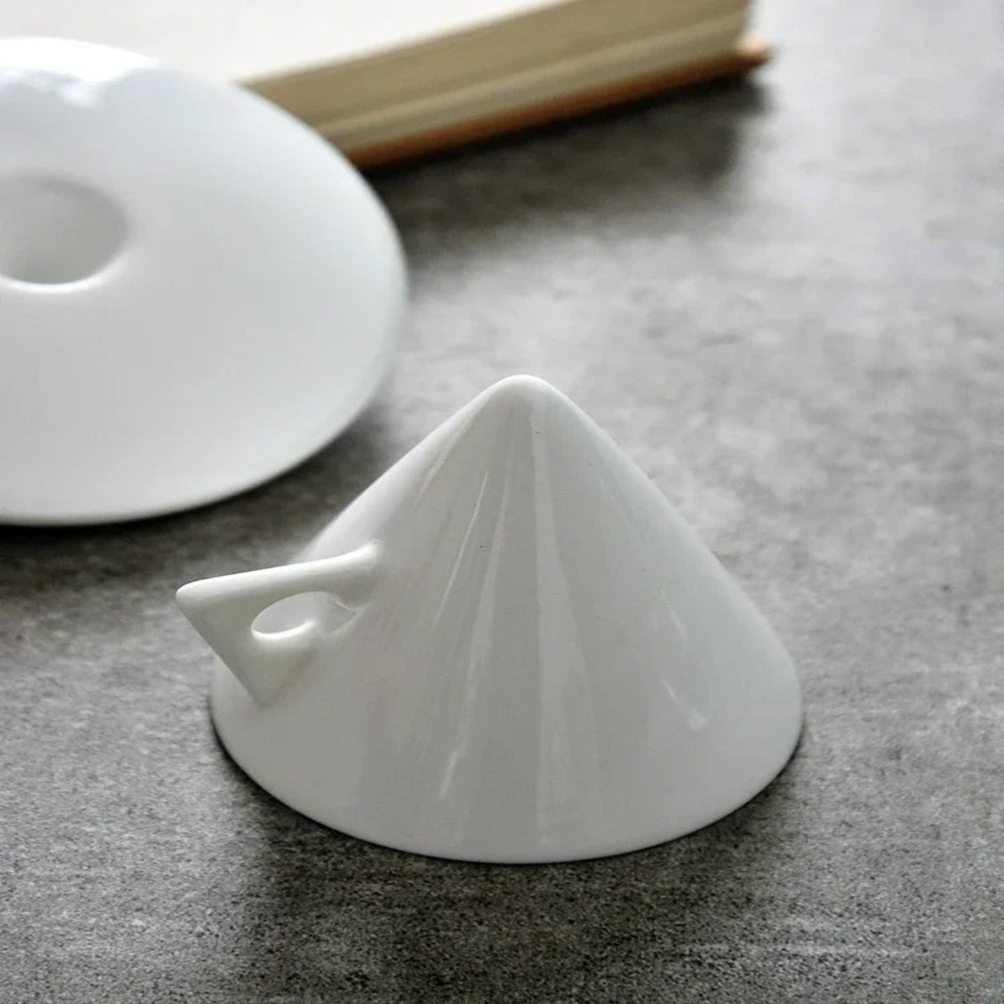 White ceramic funnel on a dark surface with a book in the background