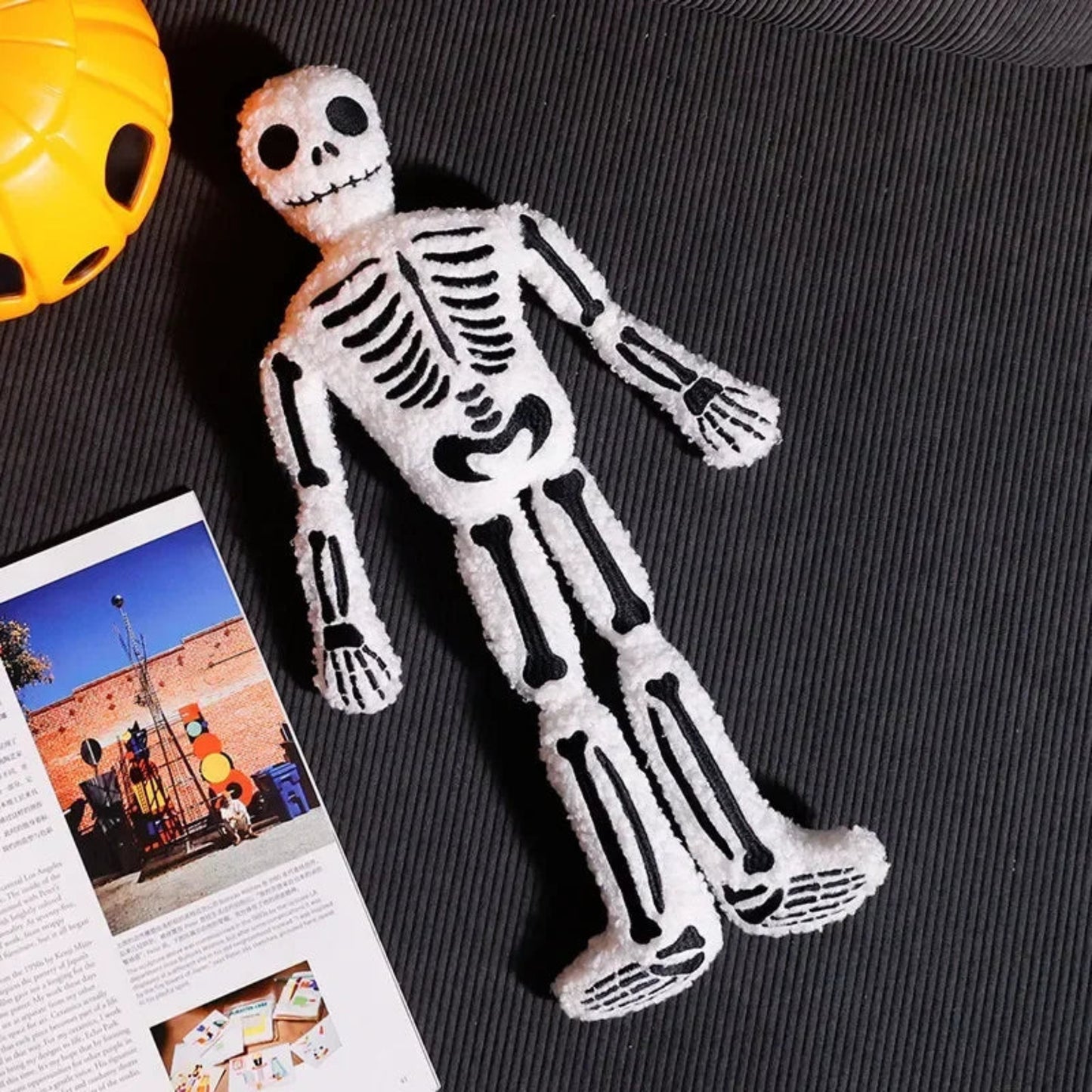 Skeleton toy on a textured surface with a magazine and yellow object in the background