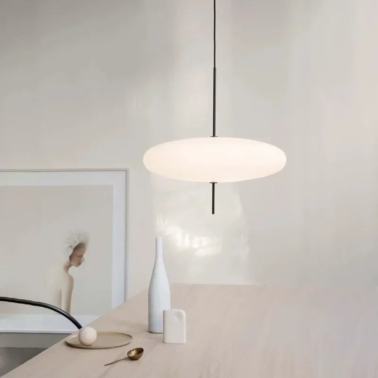 Modern pendant light hanging in a minimalistic room with a vase and decorative items on a table.