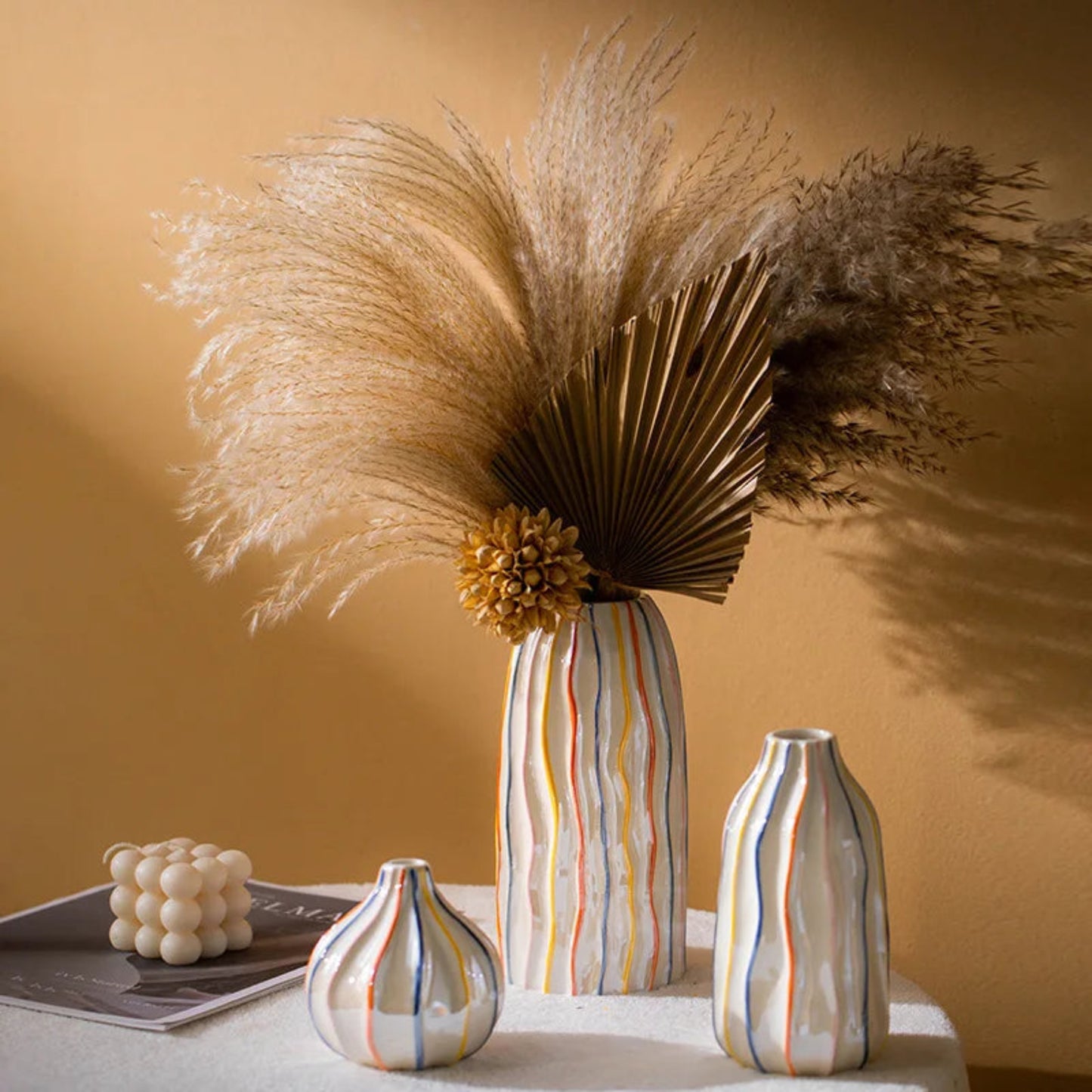 Decorative vases with striped patterns and dried pampas grass against a beige wall.