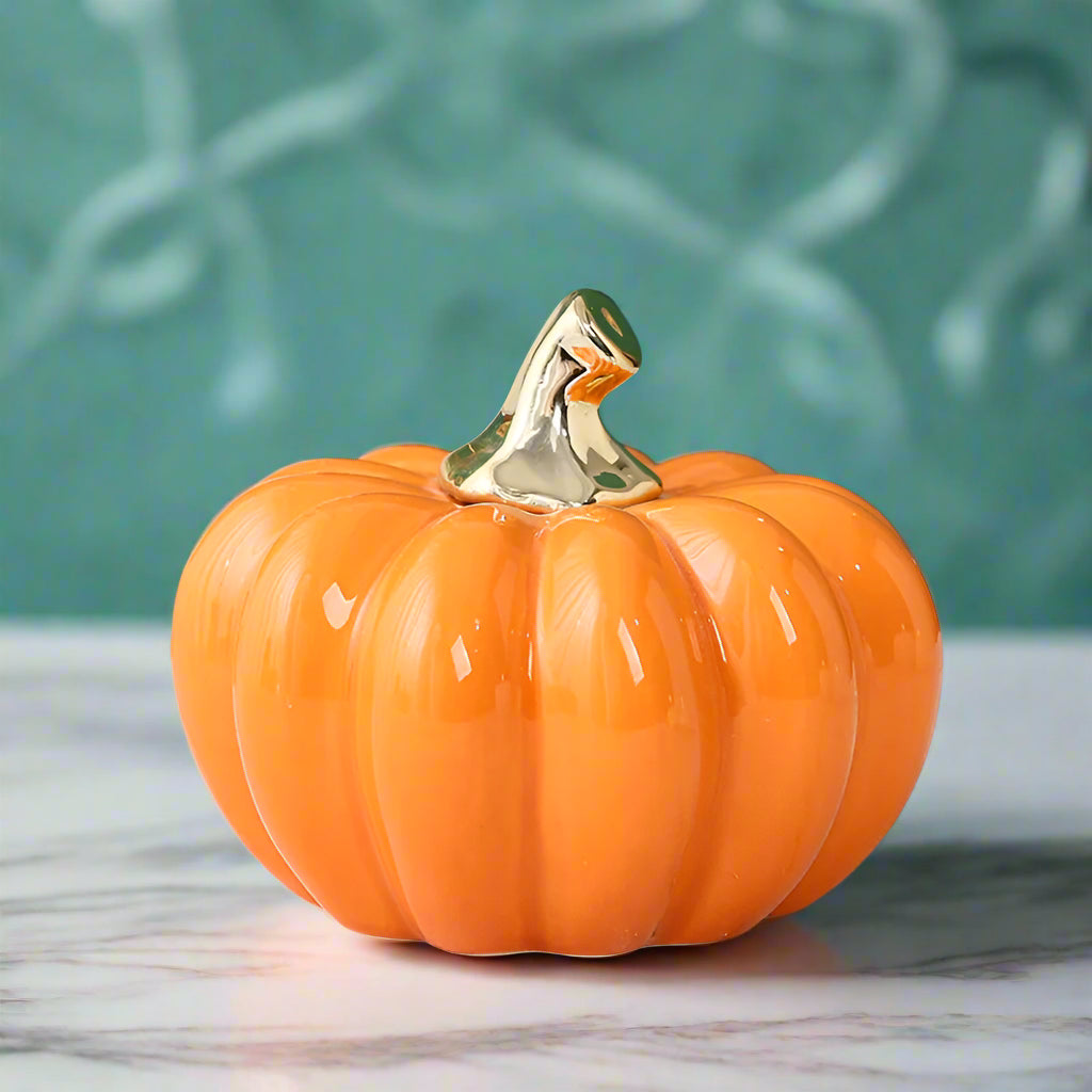Decorative pumpkin with a gold stem on a marble surface with flowers in the background