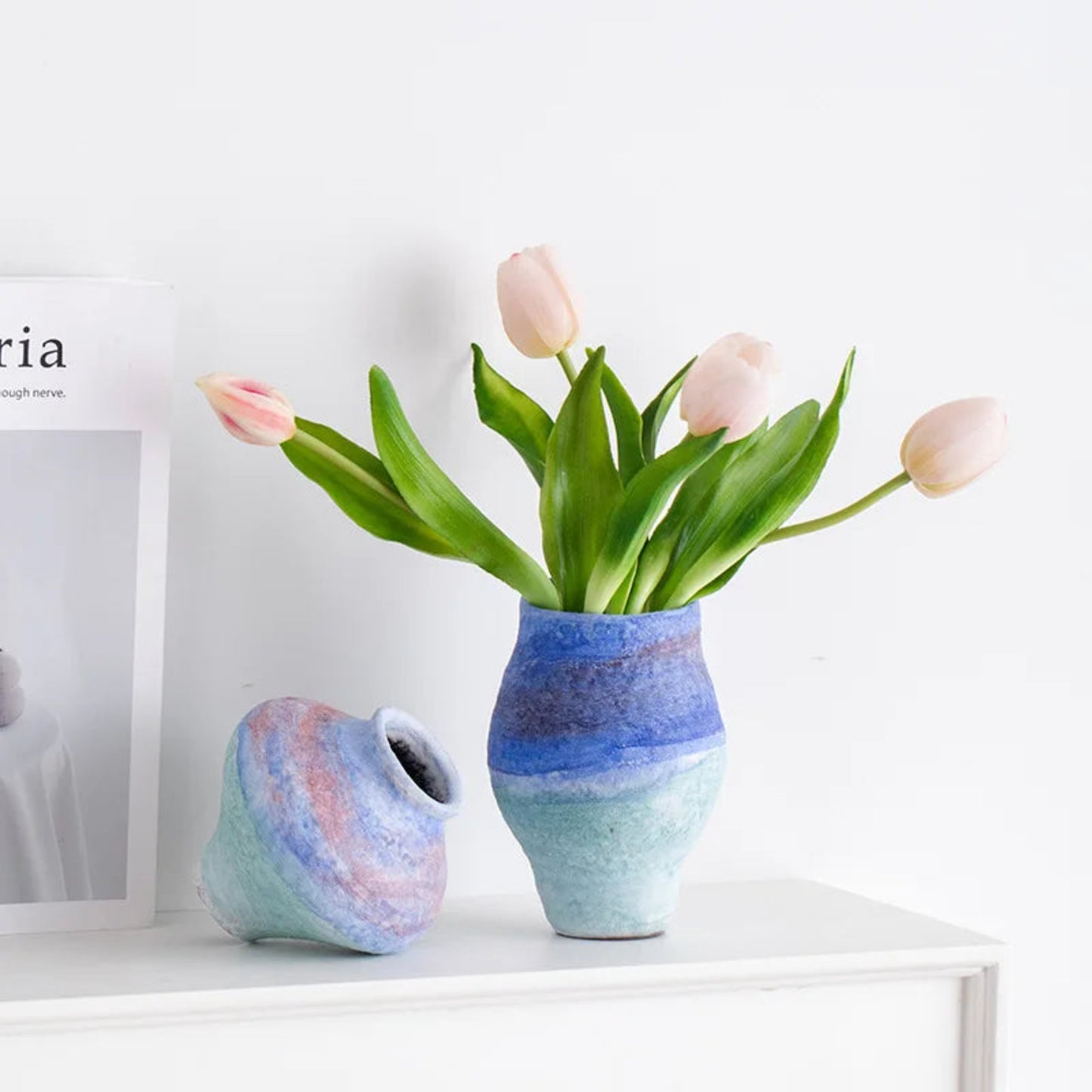 Two ceramic vases with a floral arrangement on a white surface.