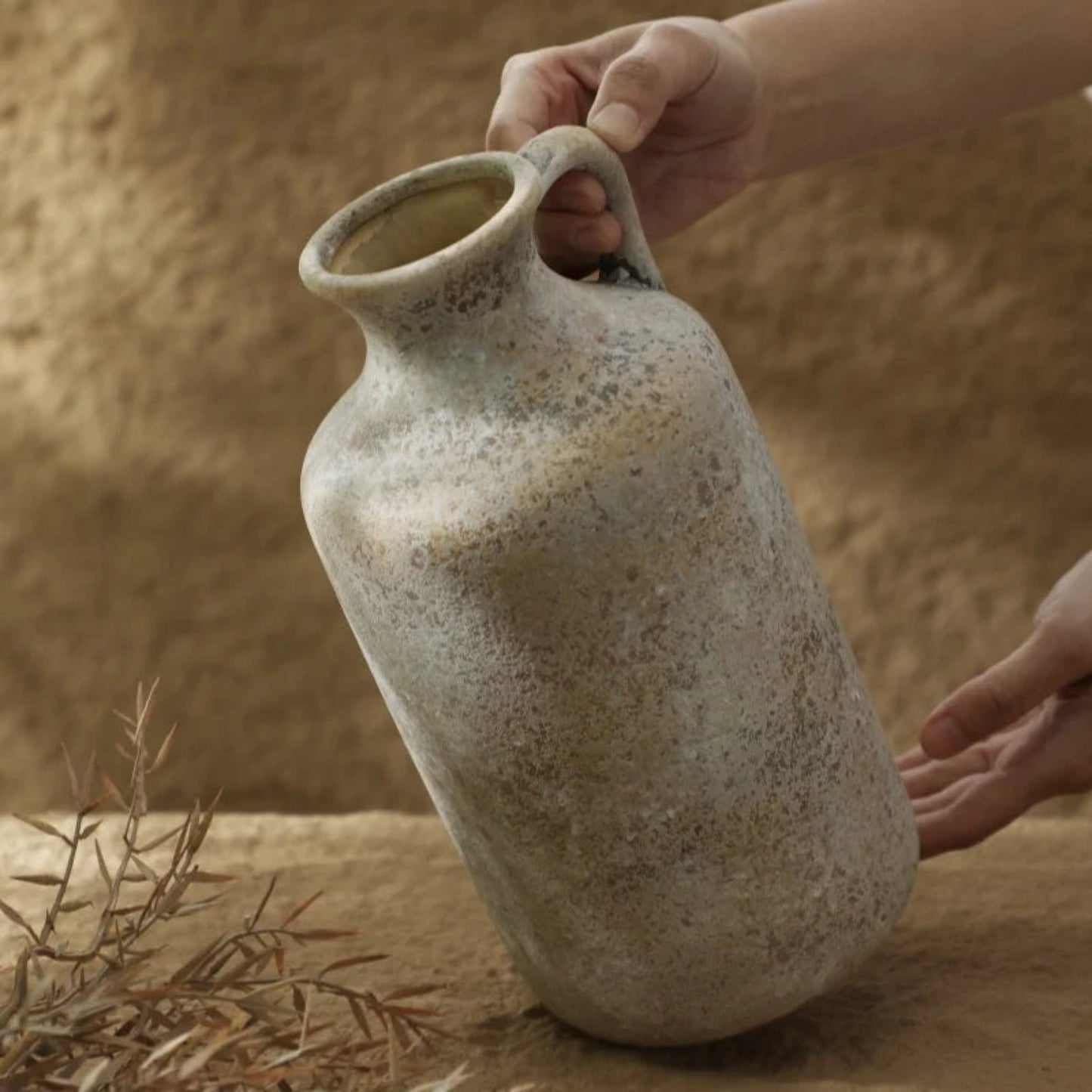 Person holding a rustic ceramic vase against a sandy background