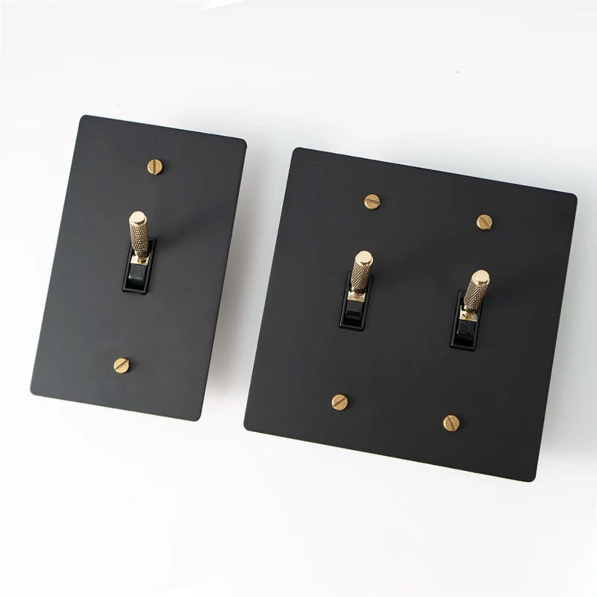 Two black light switch covers with gold screws on a white background