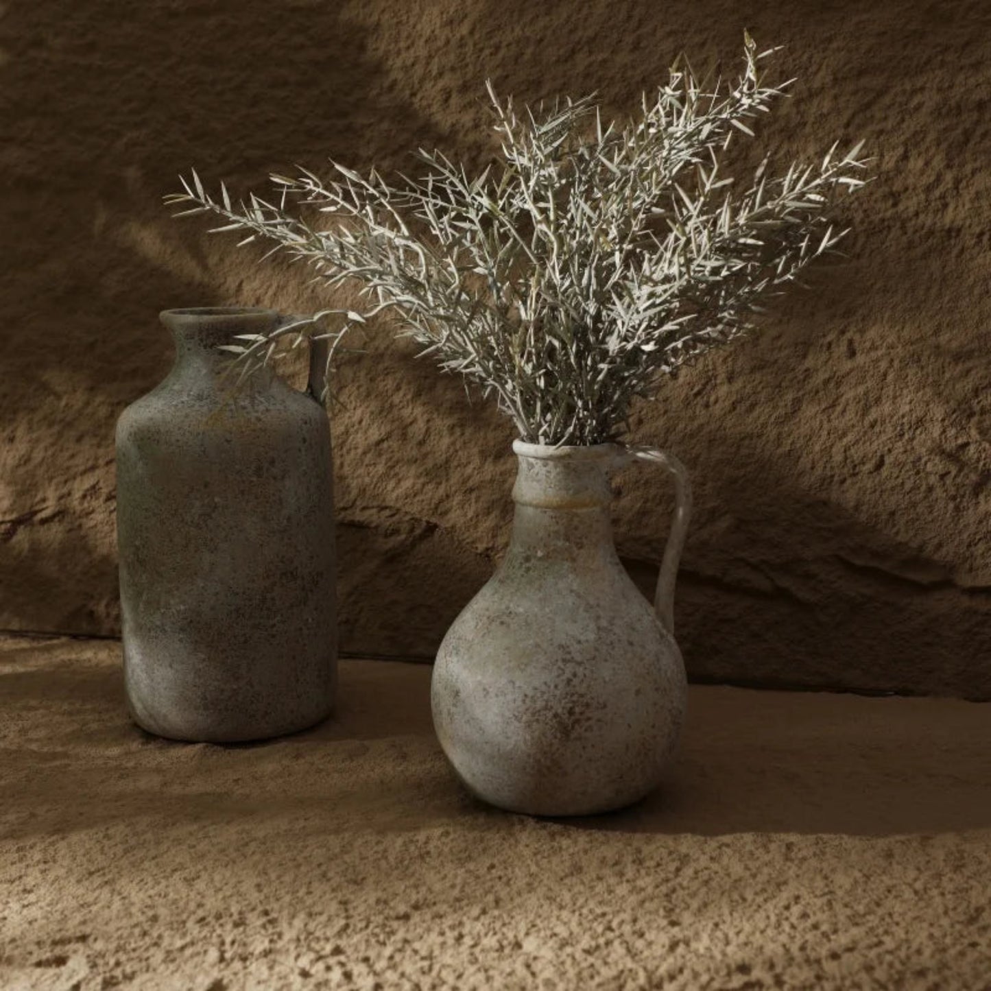 Two rustic vases with dried branches against a textured stone wall.