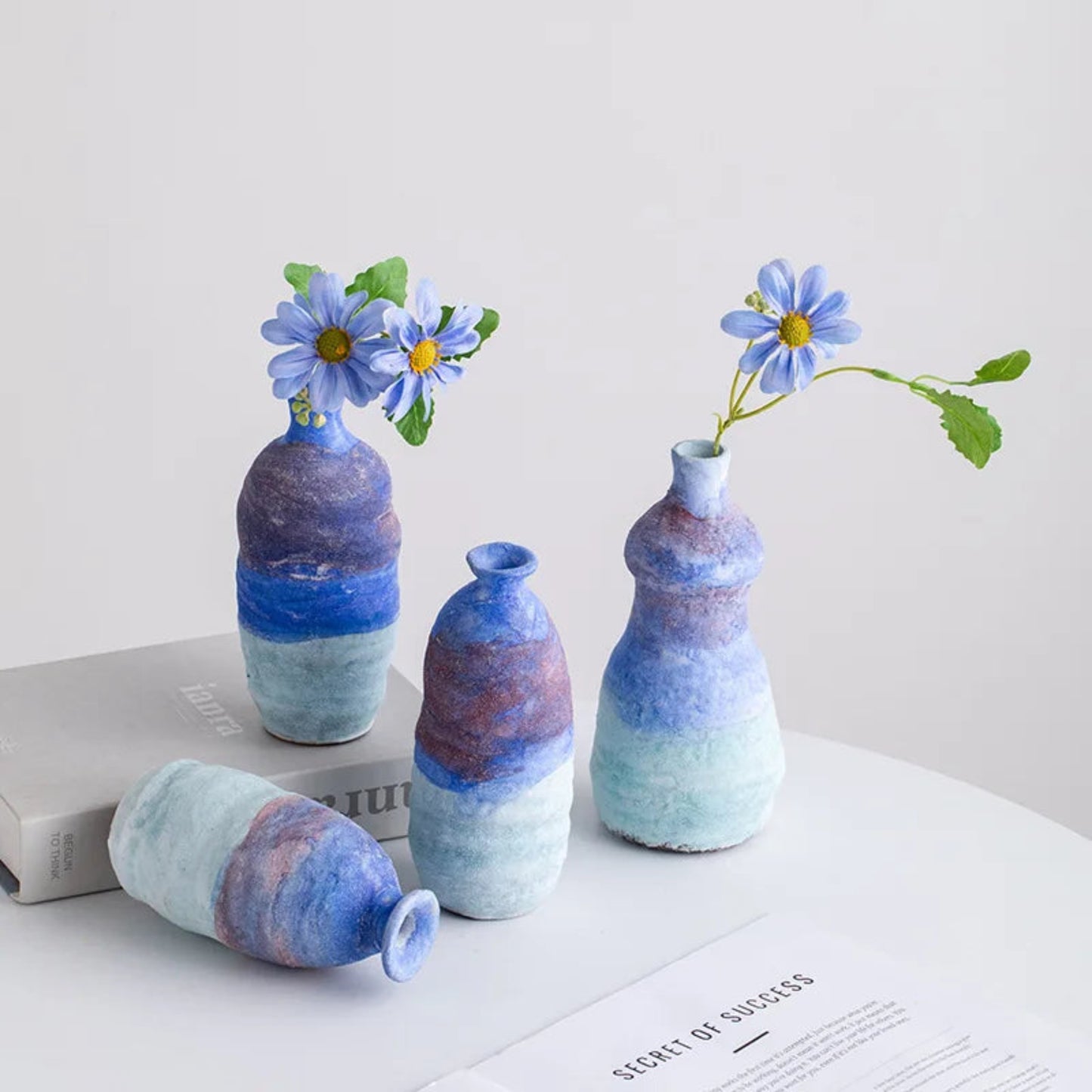 Set of four ceramic vases with blue and purple gradient, each containing a small flower arrangement on a white surface.