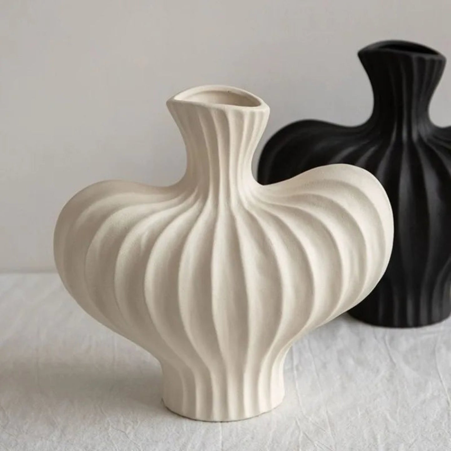 Two ceramic vases, one white and one black, on a light surface with a neutral background.