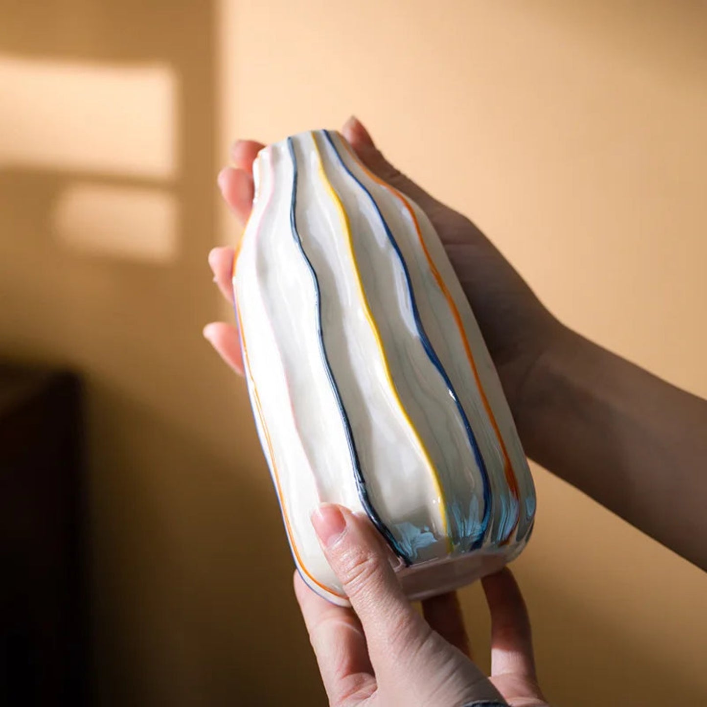 Hand holding a ceramic vase with striped design against a warm-toned background