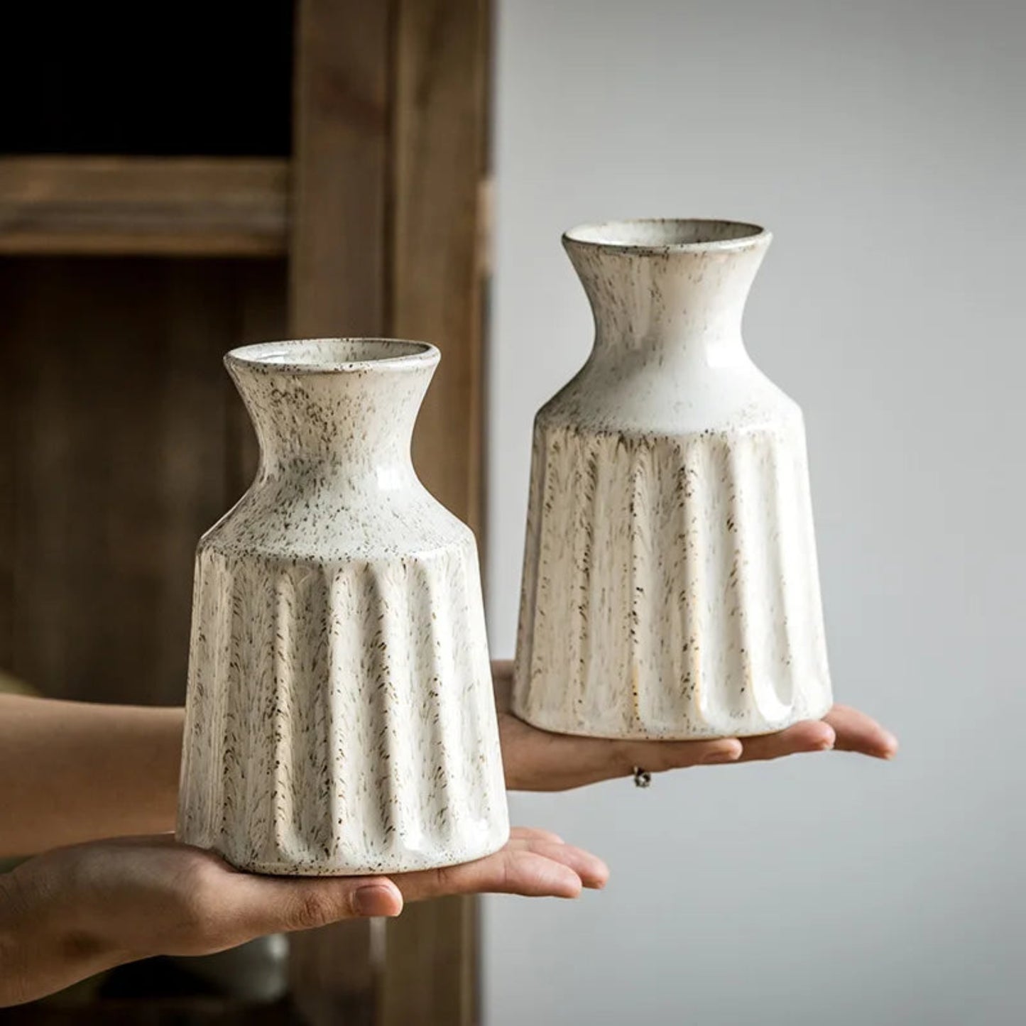 Two hands holding textured ceramic vases against a neutral background