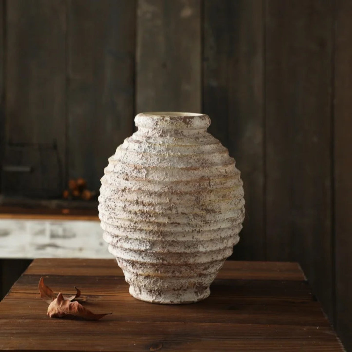 Textured ceramic vase on a wooden surface with a dark background