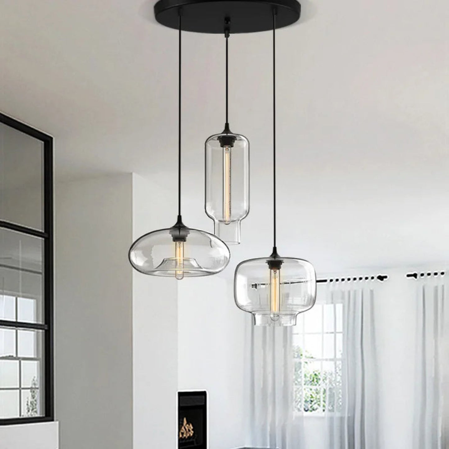 Three modern pendant lights with glass shades hanging in a room with a window and curtain.