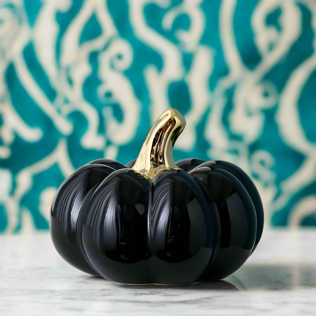 Black decorative pumpkin with a gold stem on a white surface.
