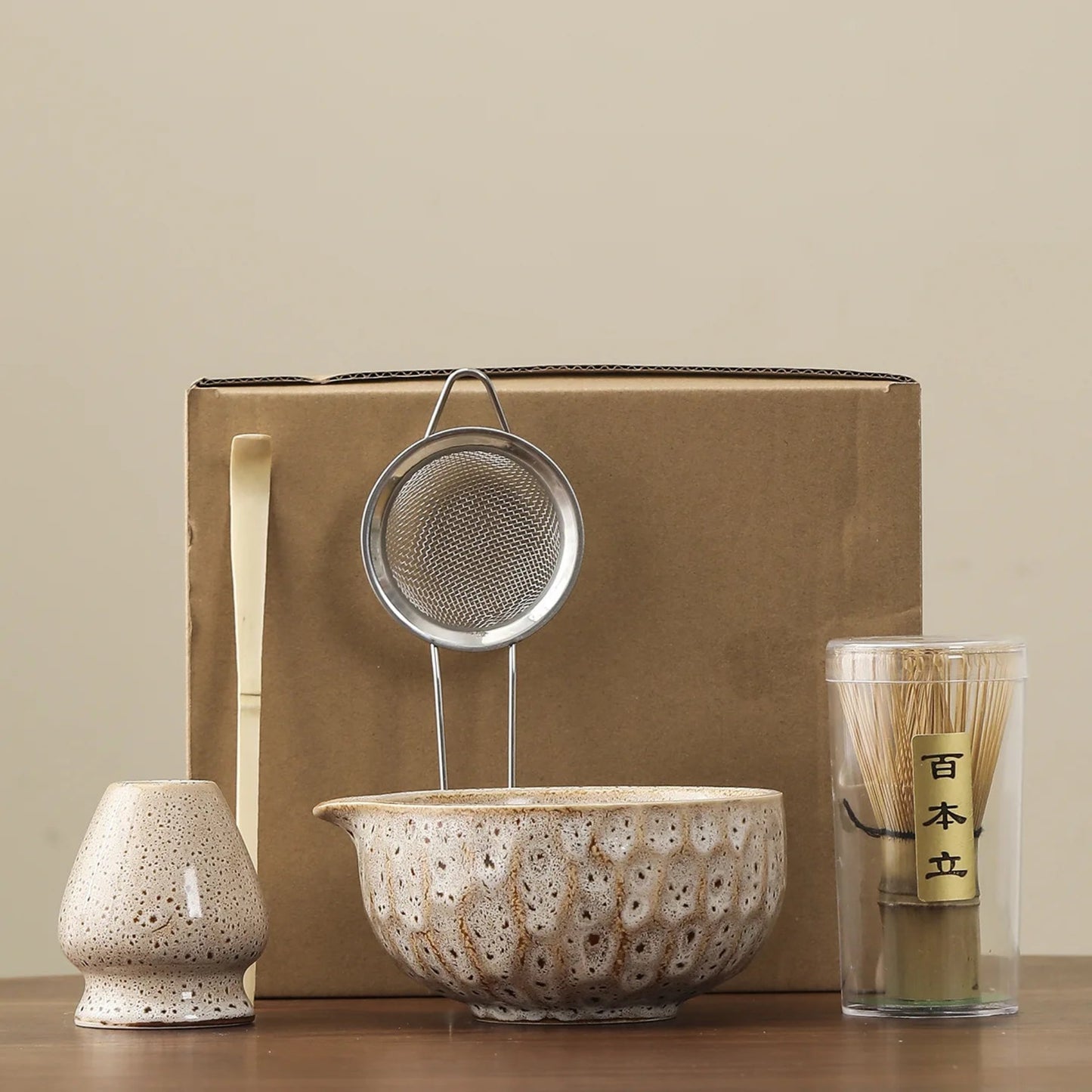 Set of ceramic and metal items including a bowl, strainer, and container with a wooden stick on a beige background.
