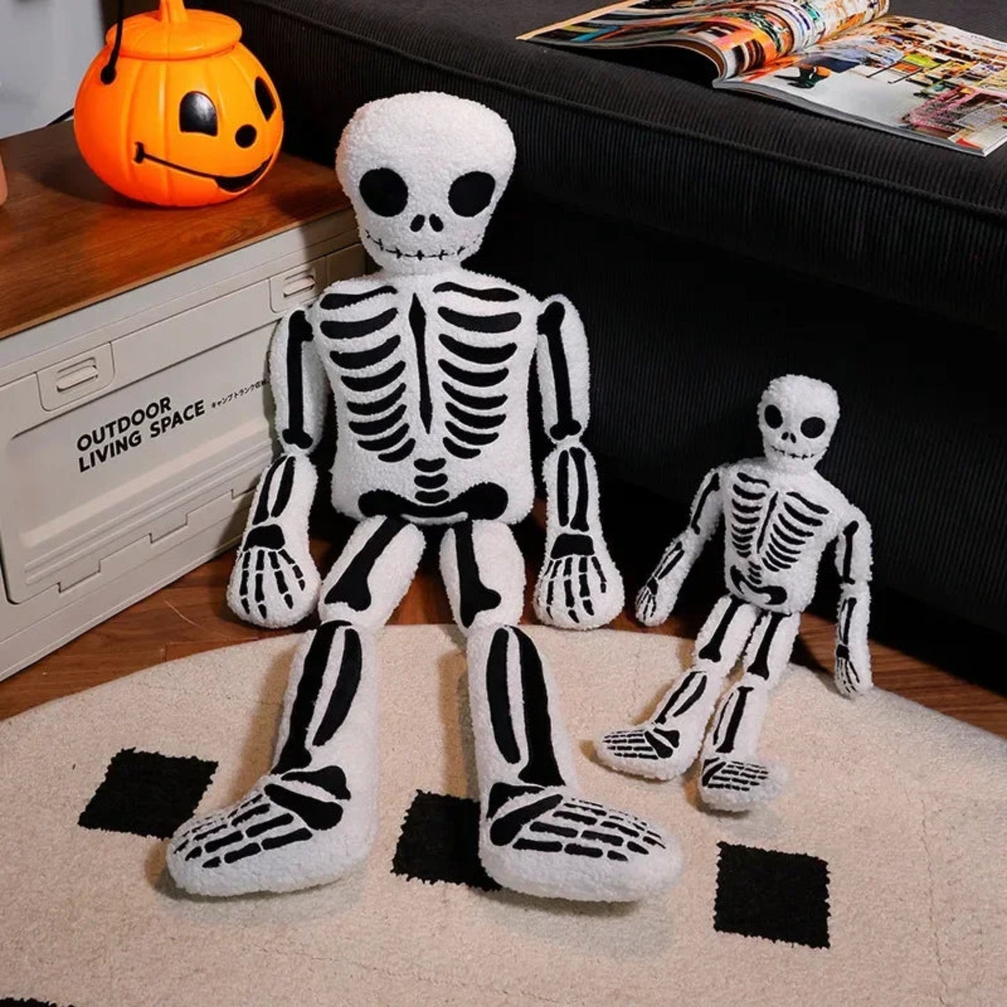 Two plush skeleton toys on a rug with Halloween decorations in the background.