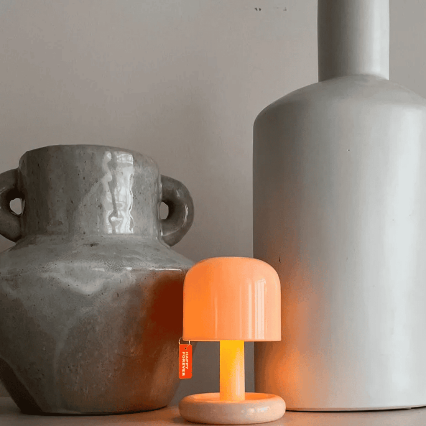 Small orange lamp with a white base between two gray vases on a neutral background