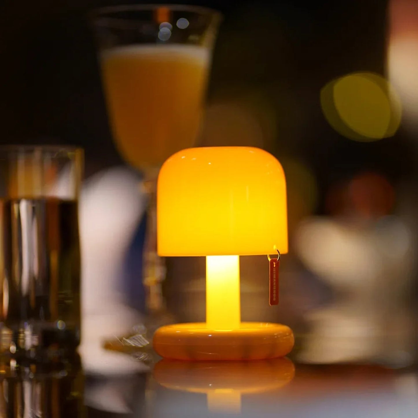Small yellow lamp on a bar counter with glasses of drinks in the background
