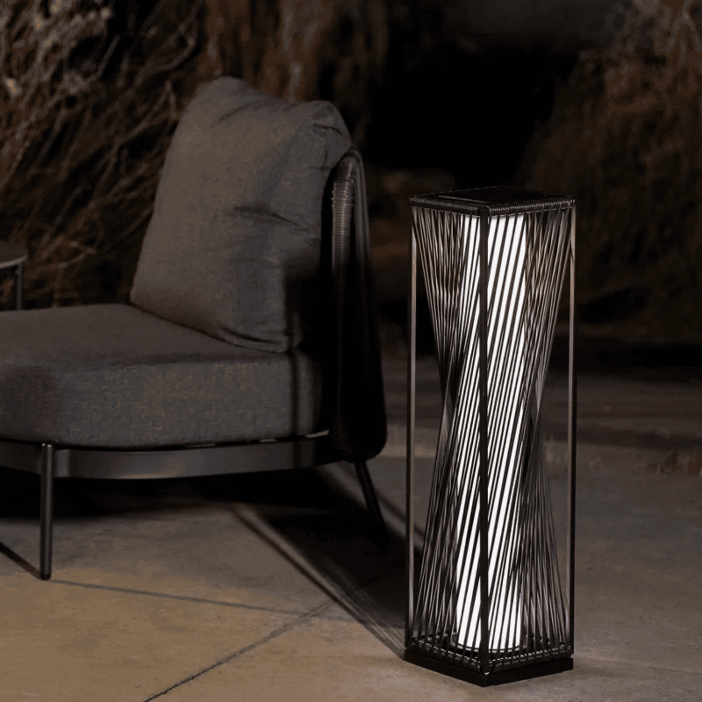 Decorative black pedestal with wavy design next to a gray cushioned chair in a dimly lit room.