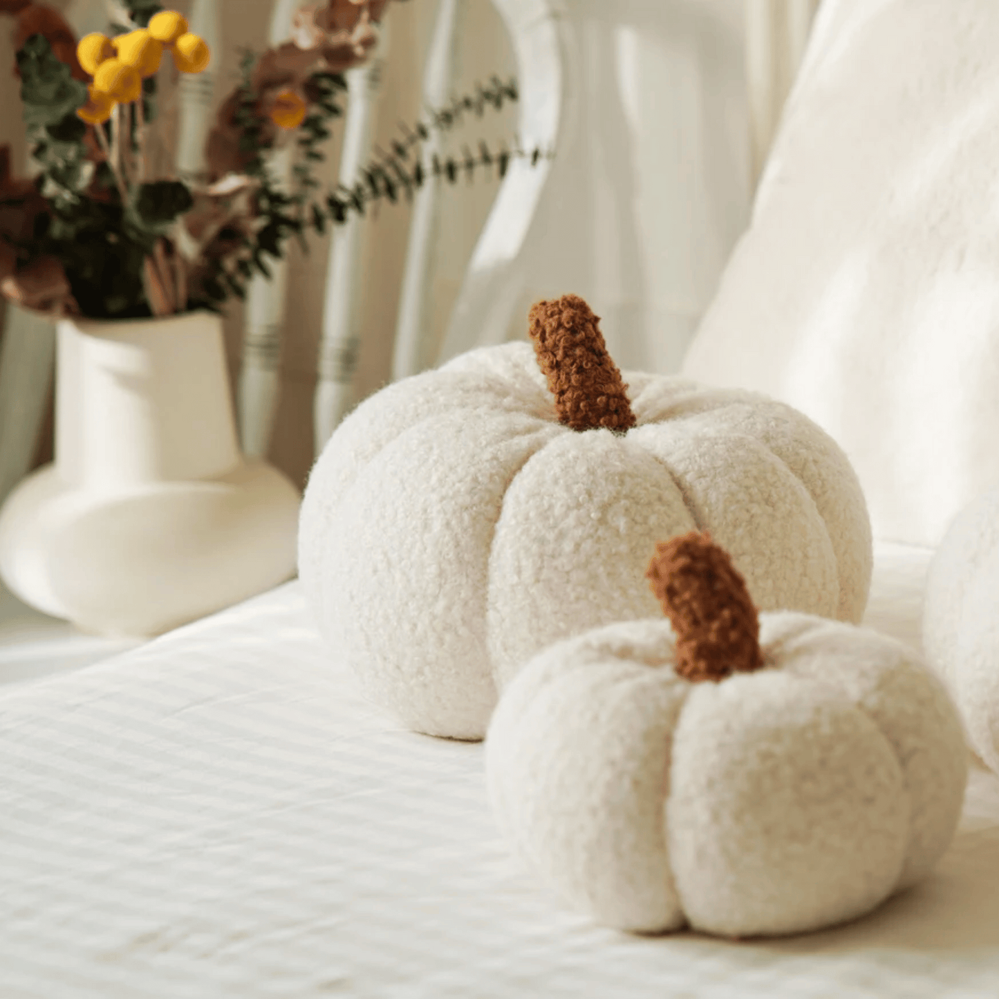 Two white textured pumpkins with brown stems on a light surface.
