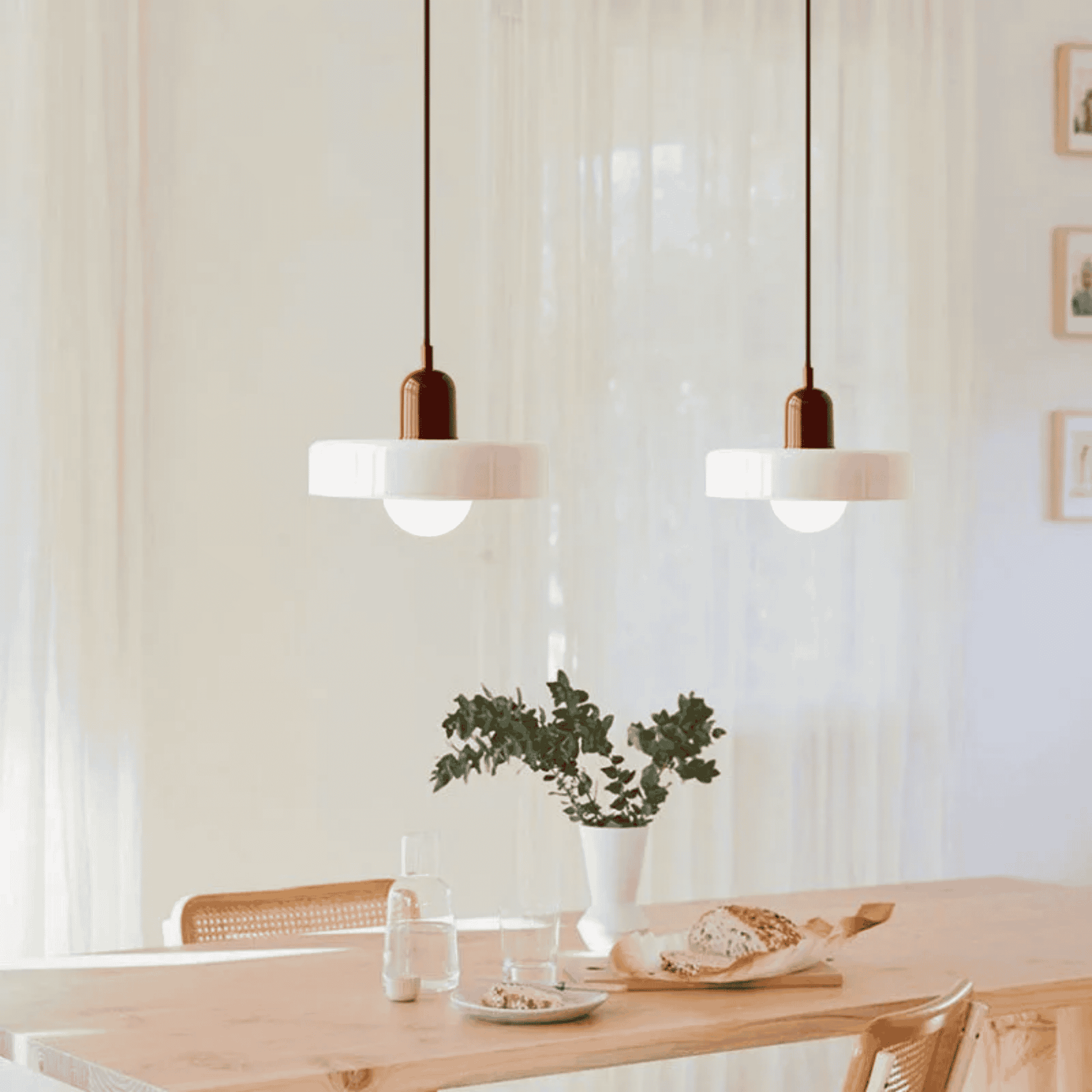 Modern pendant lights hanging above a dining table with a plant and decor items.