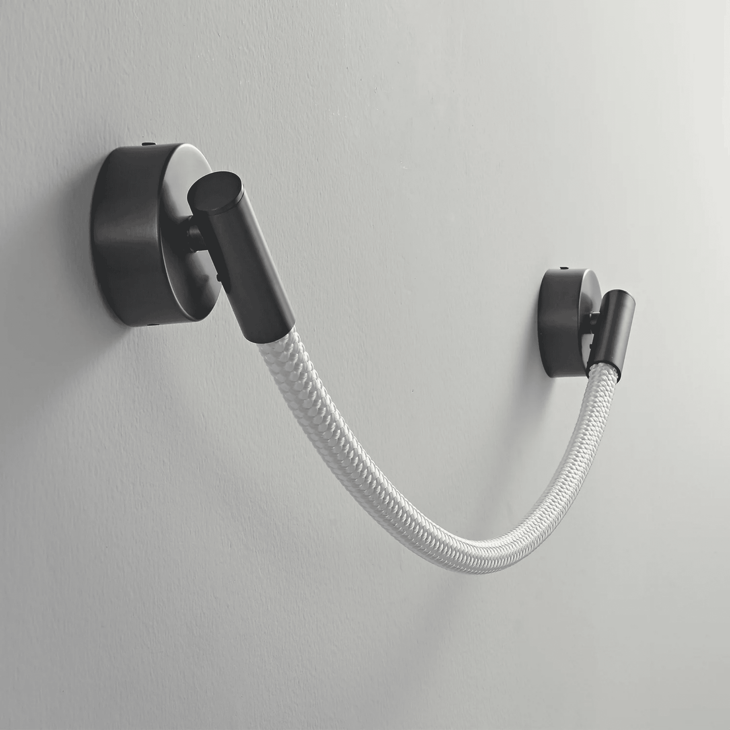 Black wall-mounted lamp with a flexible white hose on a gray background