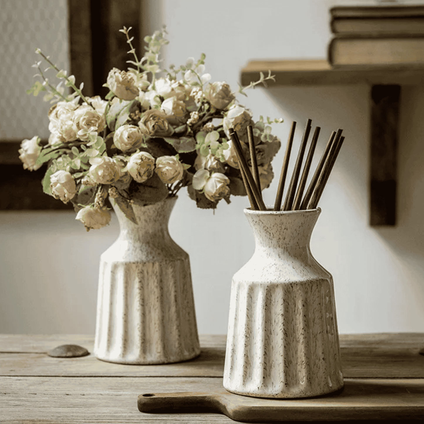 Two ceramic vases with a bouquet of flowers and reed diffuser on a wooden surface.