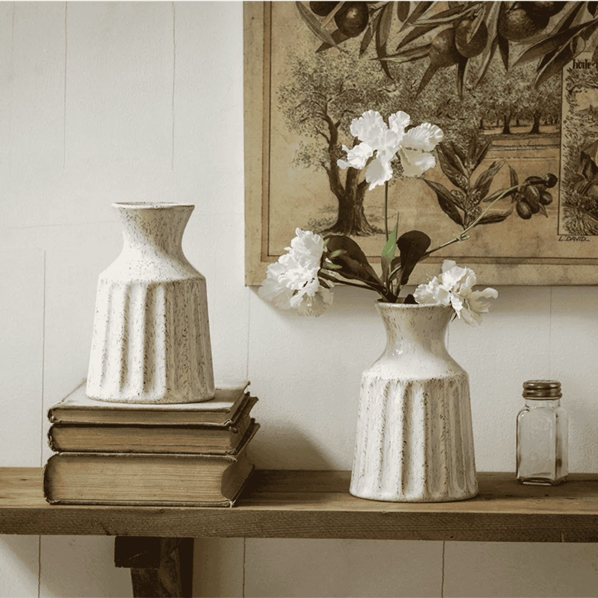 Decorative setting with a textured vase, stack of books, and a small jar on a shelf.