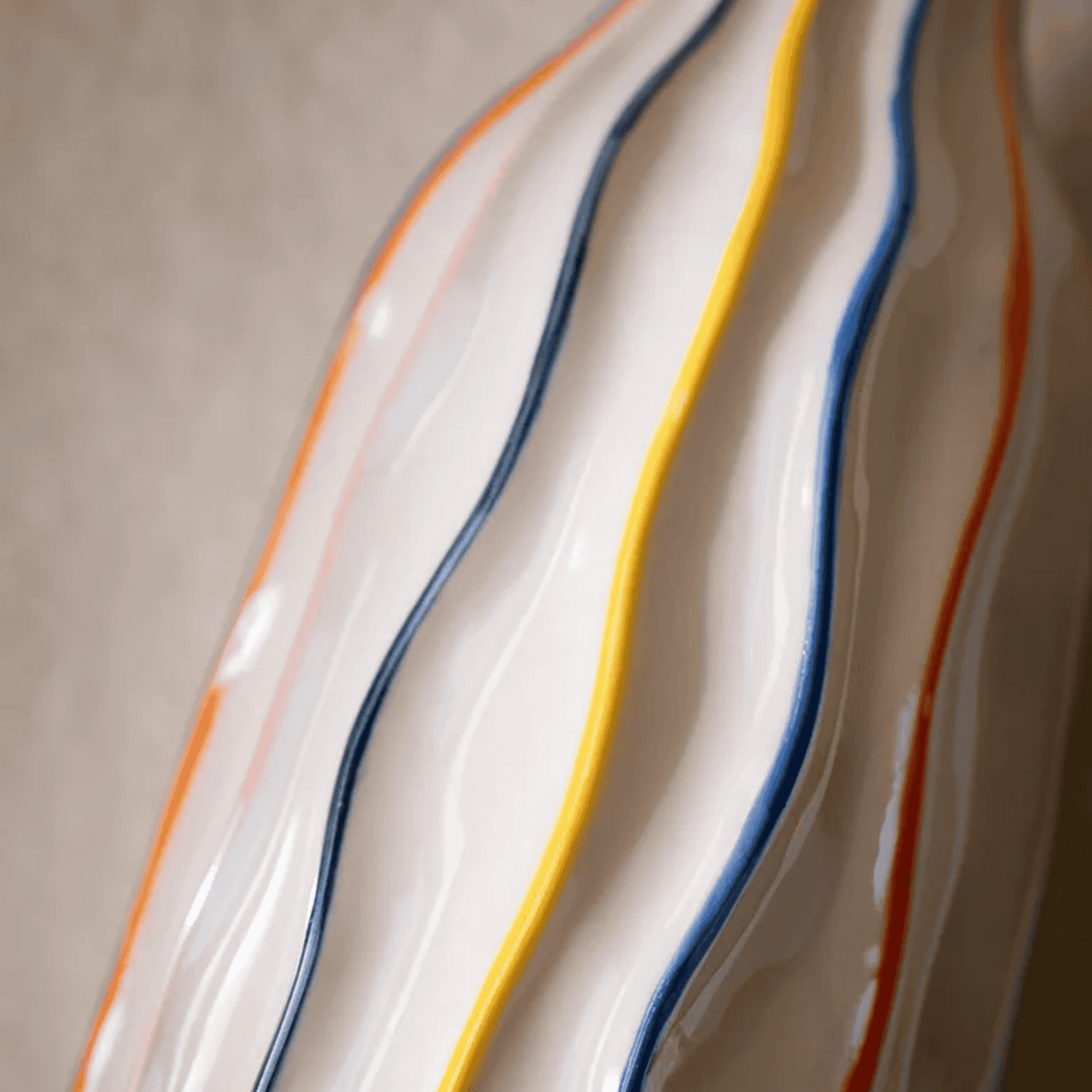 Close-up of a ceramic plate with wavy design and colorful stripes on a neutral background