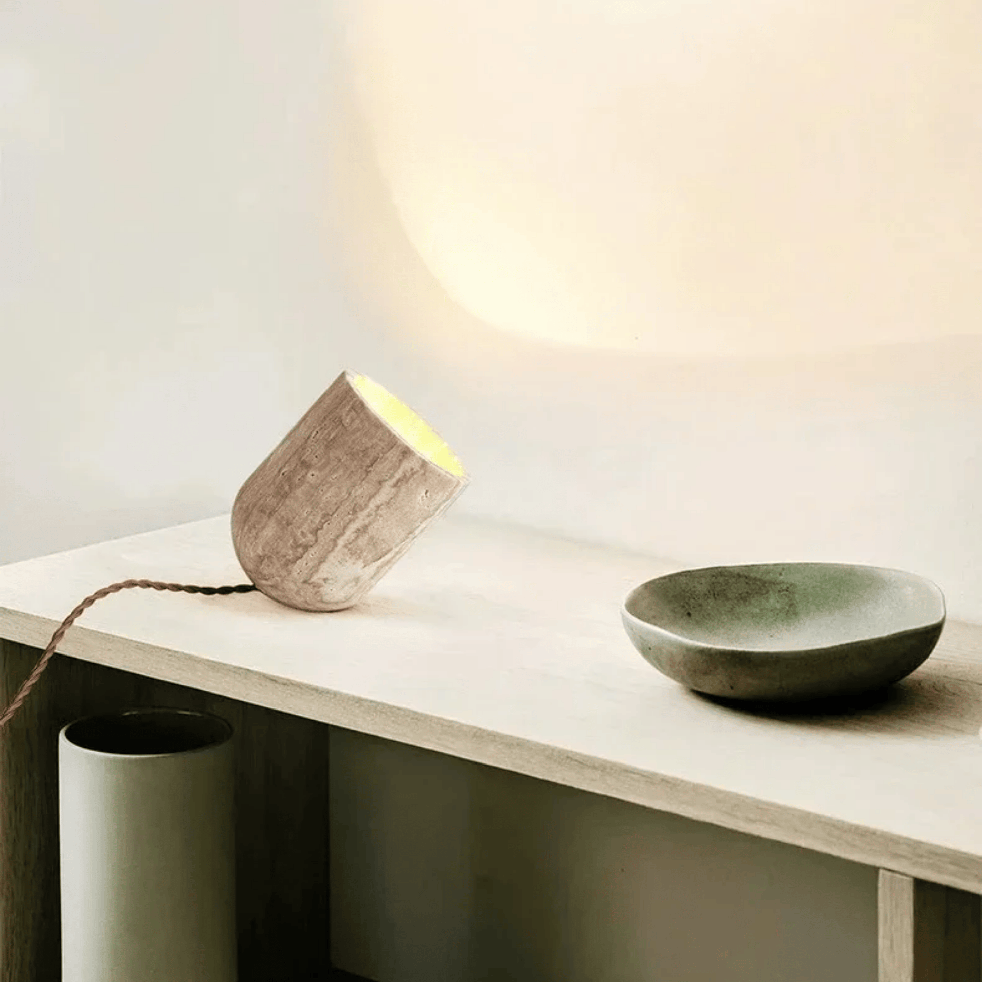 Concrete lamp and bowl on a wooden surface with a soft light in the background