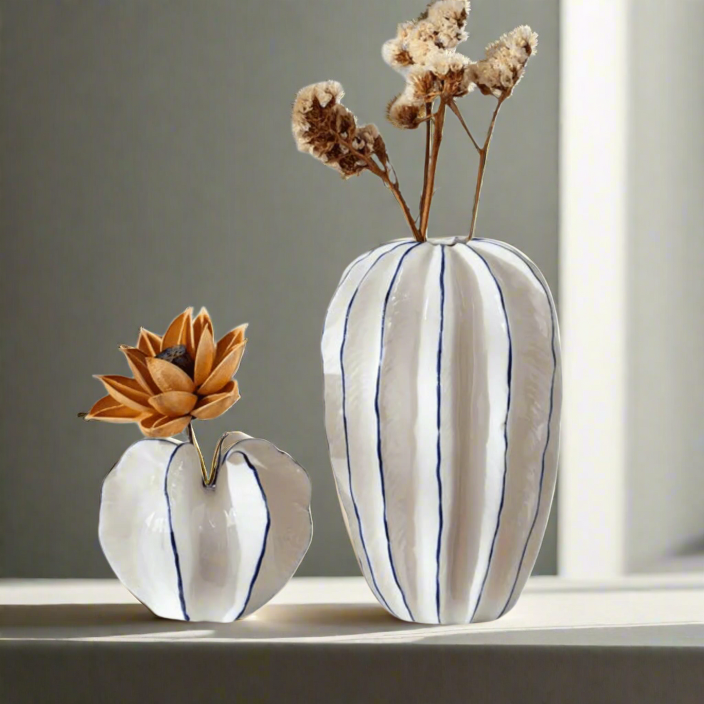 Two ceramic vases with striped patterns and dried flowers on a white background