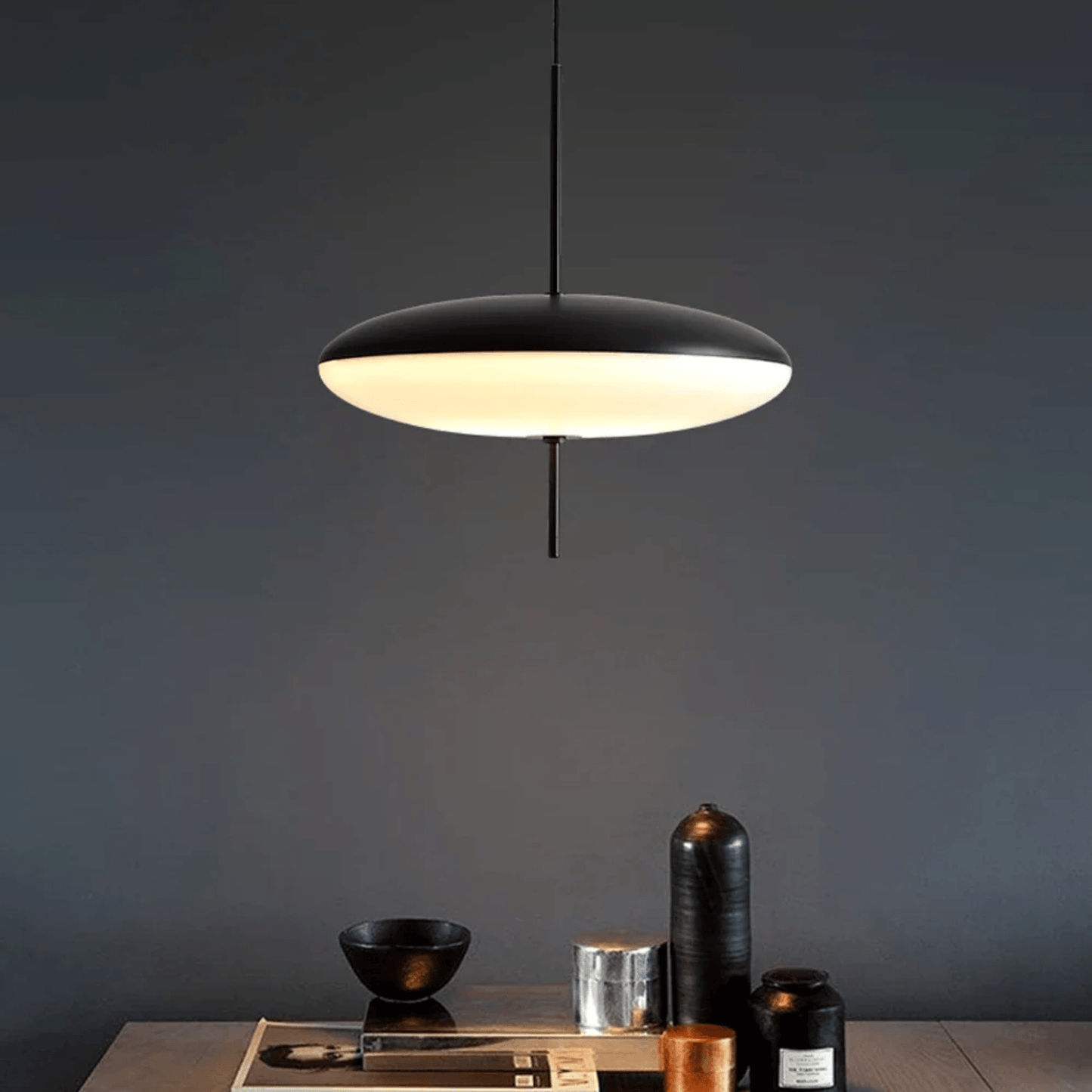 Modern pendant light hanging above a table with decorative items against a dark wall.