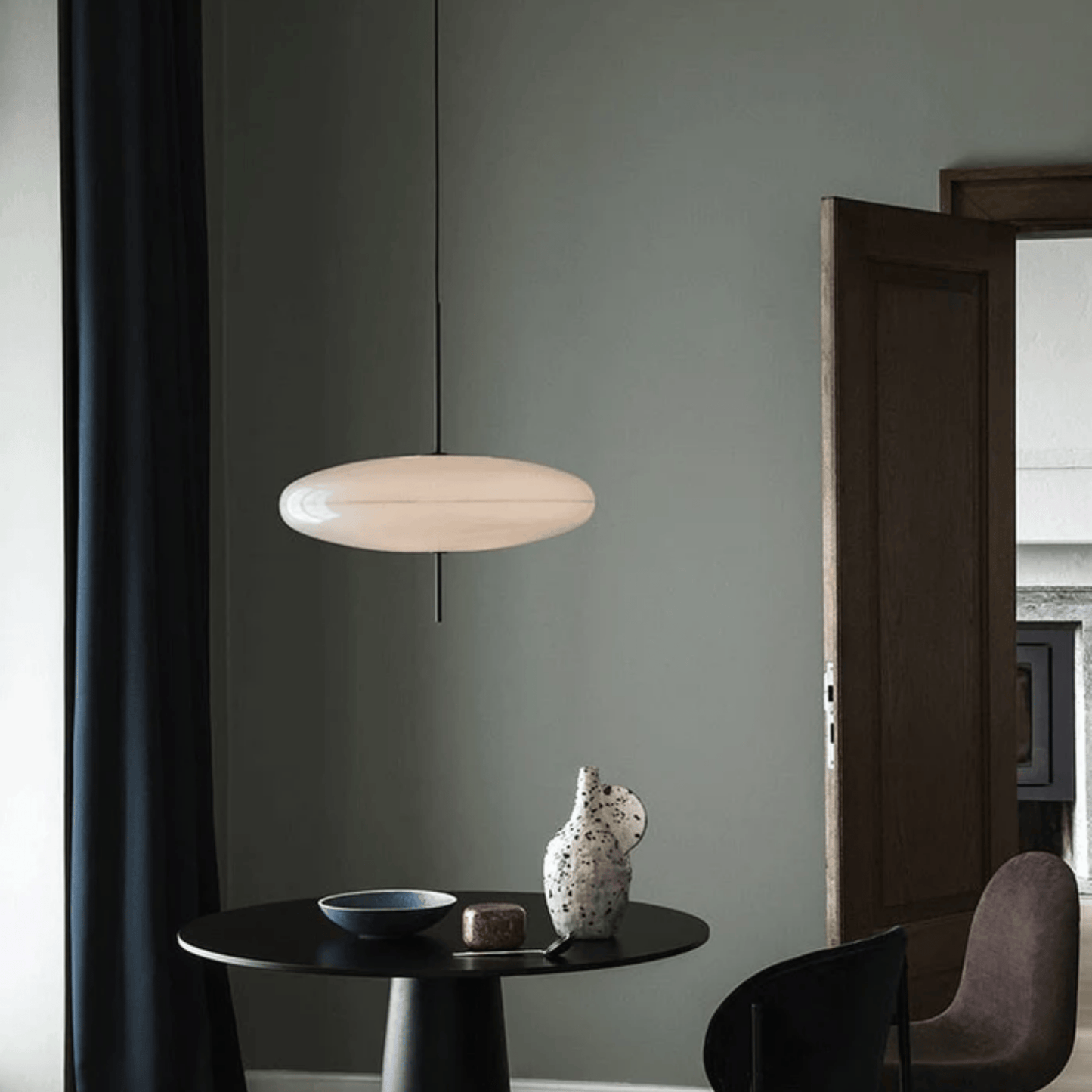Modern pendant light hanging above a table with decorative items against a gray wall.