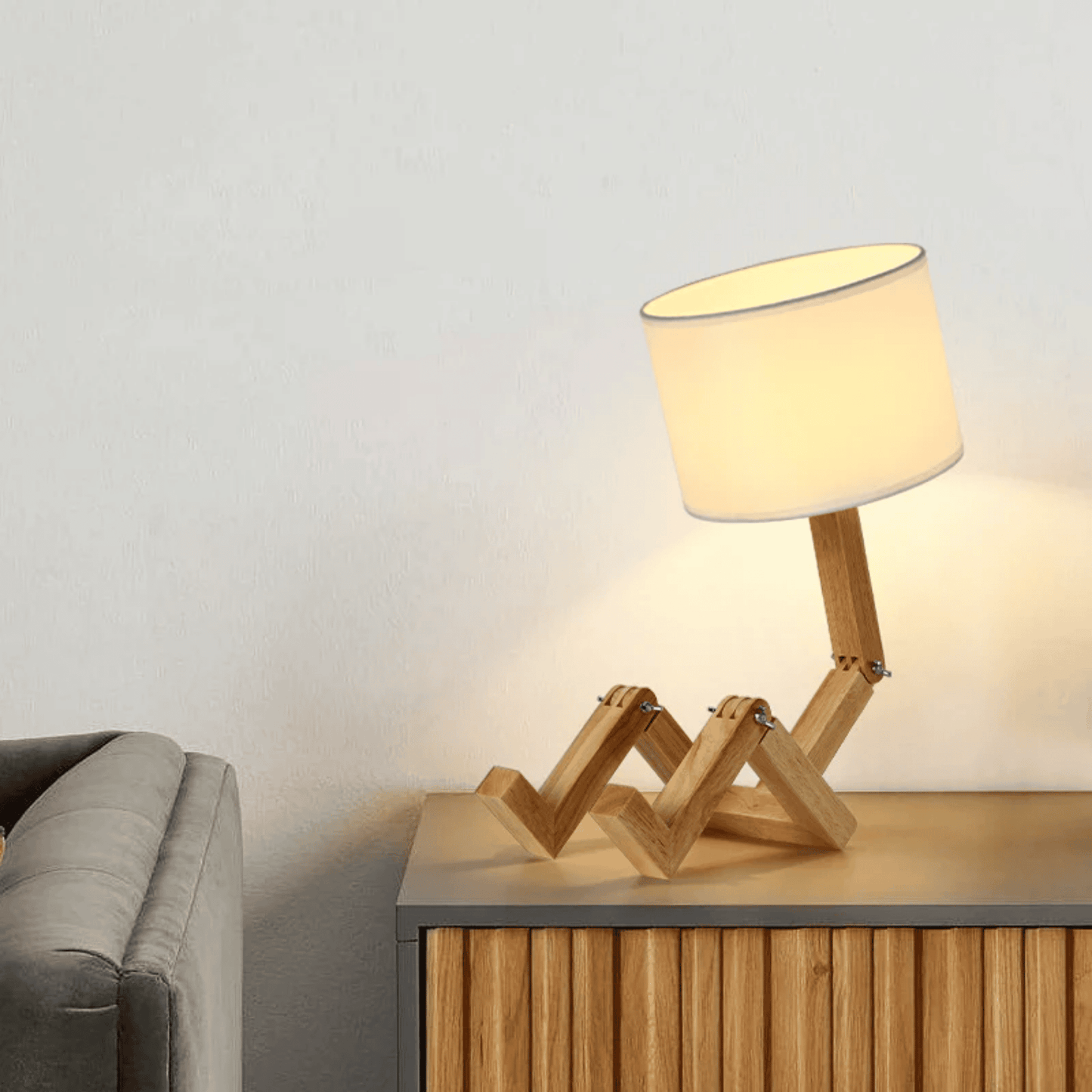 Wooden lamp with a white shade on a wooden side table next to a gray sofa.