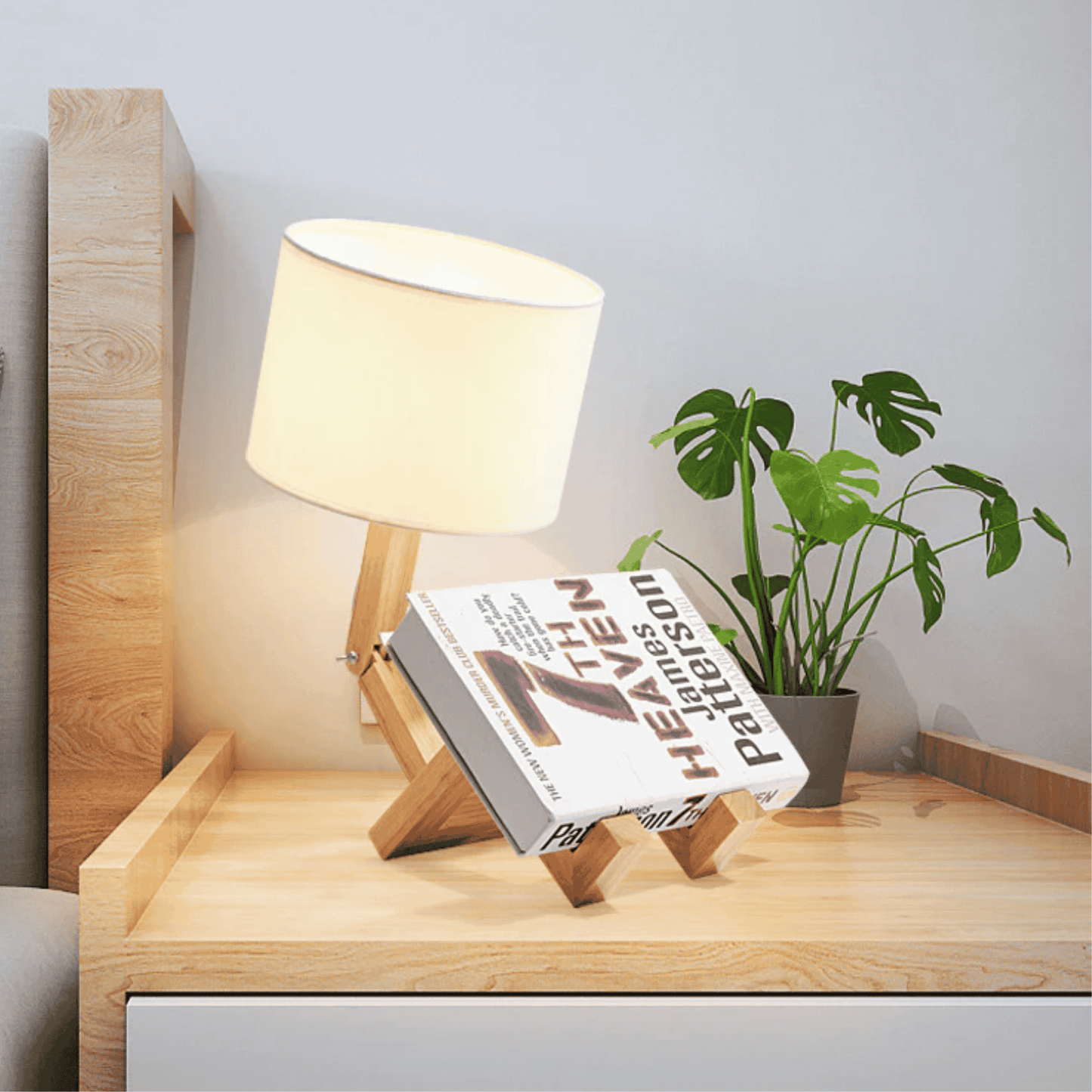 Wooden lamp with a book stand holding an open book on a wooden surface with a plant in the background.