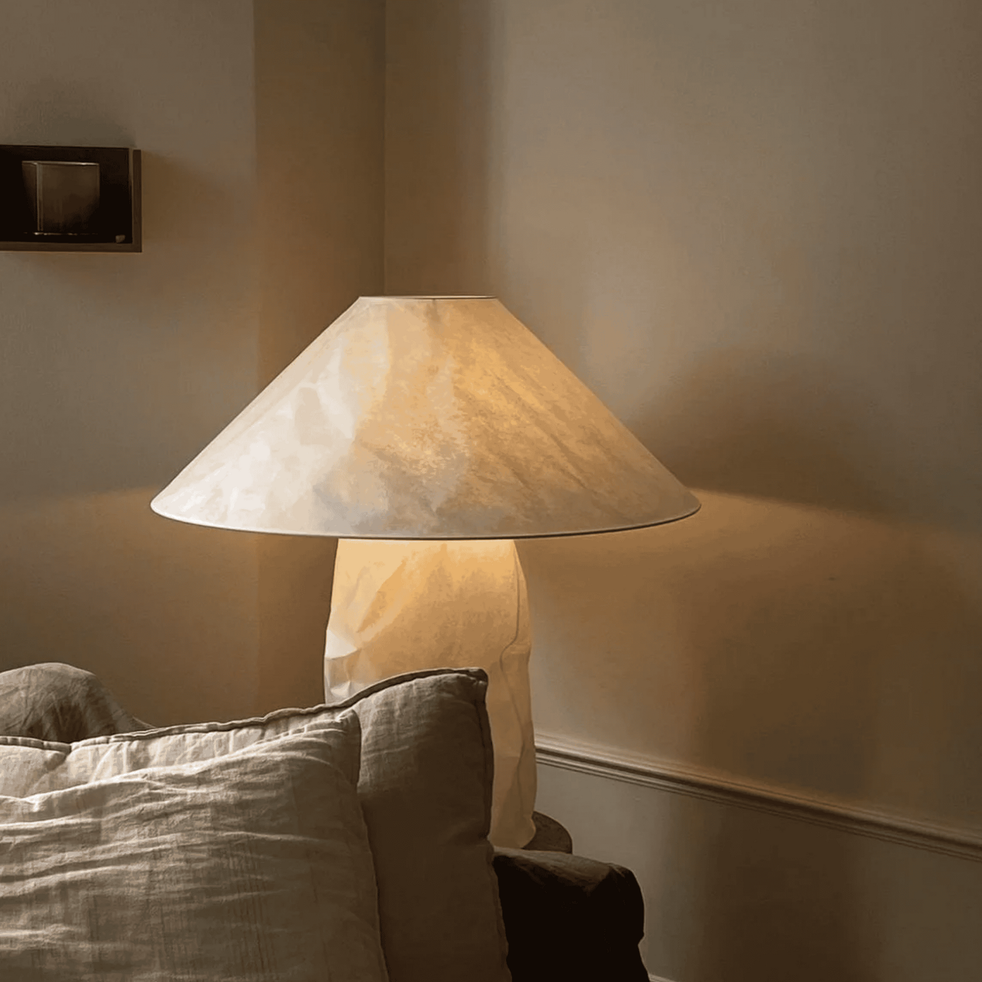 Lamp with a soft glow on a surface next to a textured pillow against a neutral wall.