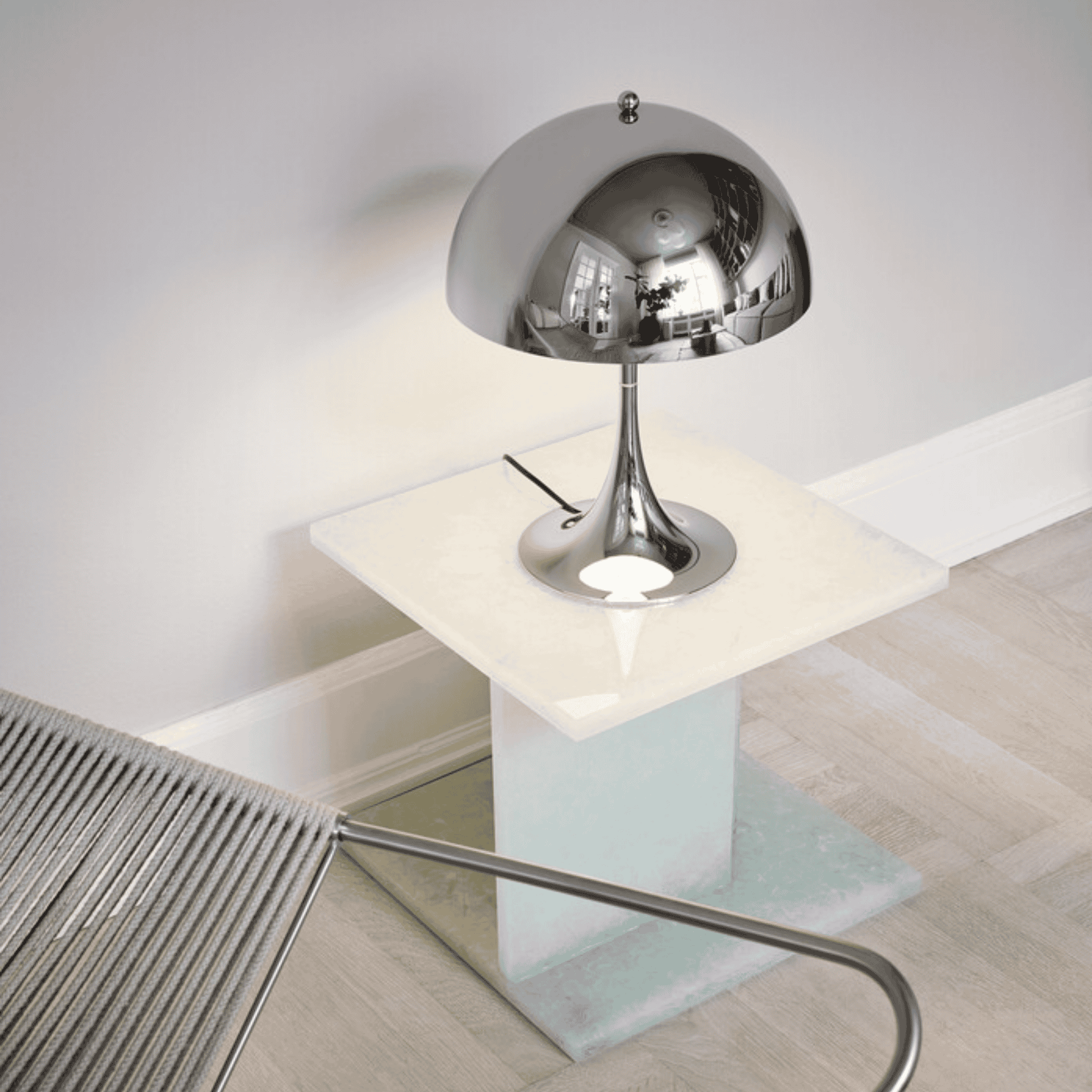 Modern silver table lamp on a glass table with a chair in the background