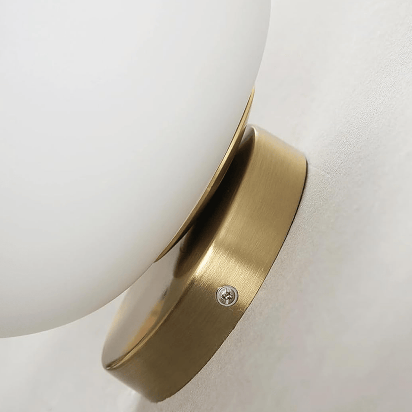 Wall-mounted light fixture with white shade and gold metal base on a neutral background