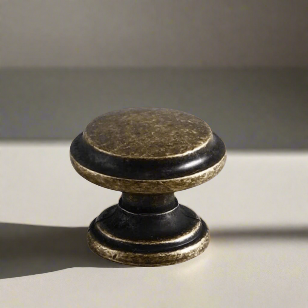 Decorative cabinet knob with black and gold finish on a beige background