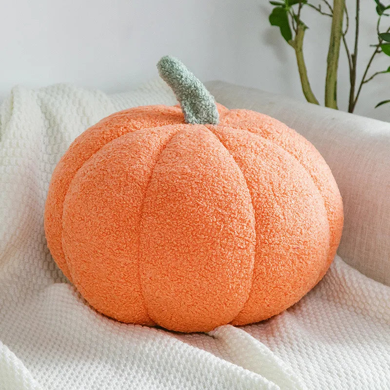 Plush pumpkin toy on a white blanket with a plant in the background