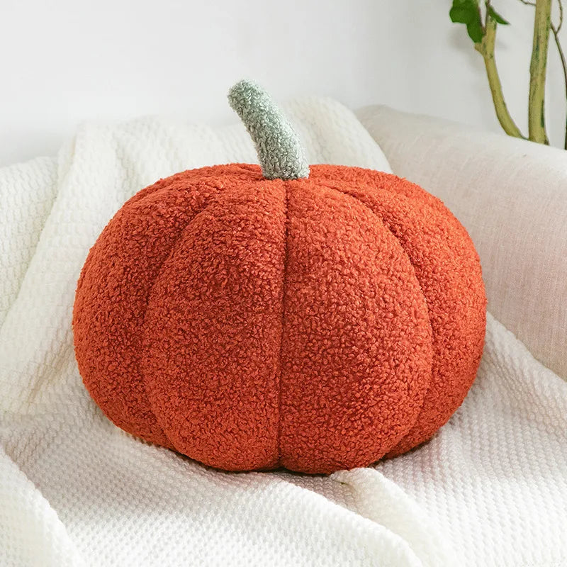 Plush pumpkin pillow on a white blanket with a plant in the background