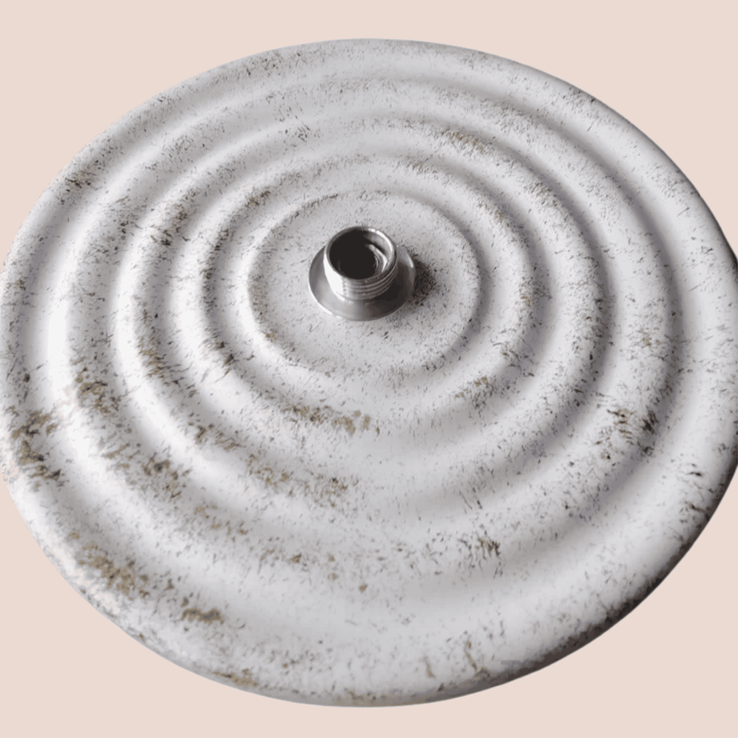 Round metallic object with concentric circles and a central hole on a beige background