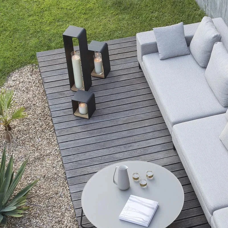 Outdoor patio with gray sofa, small table, and candle holders on a wooden deck.