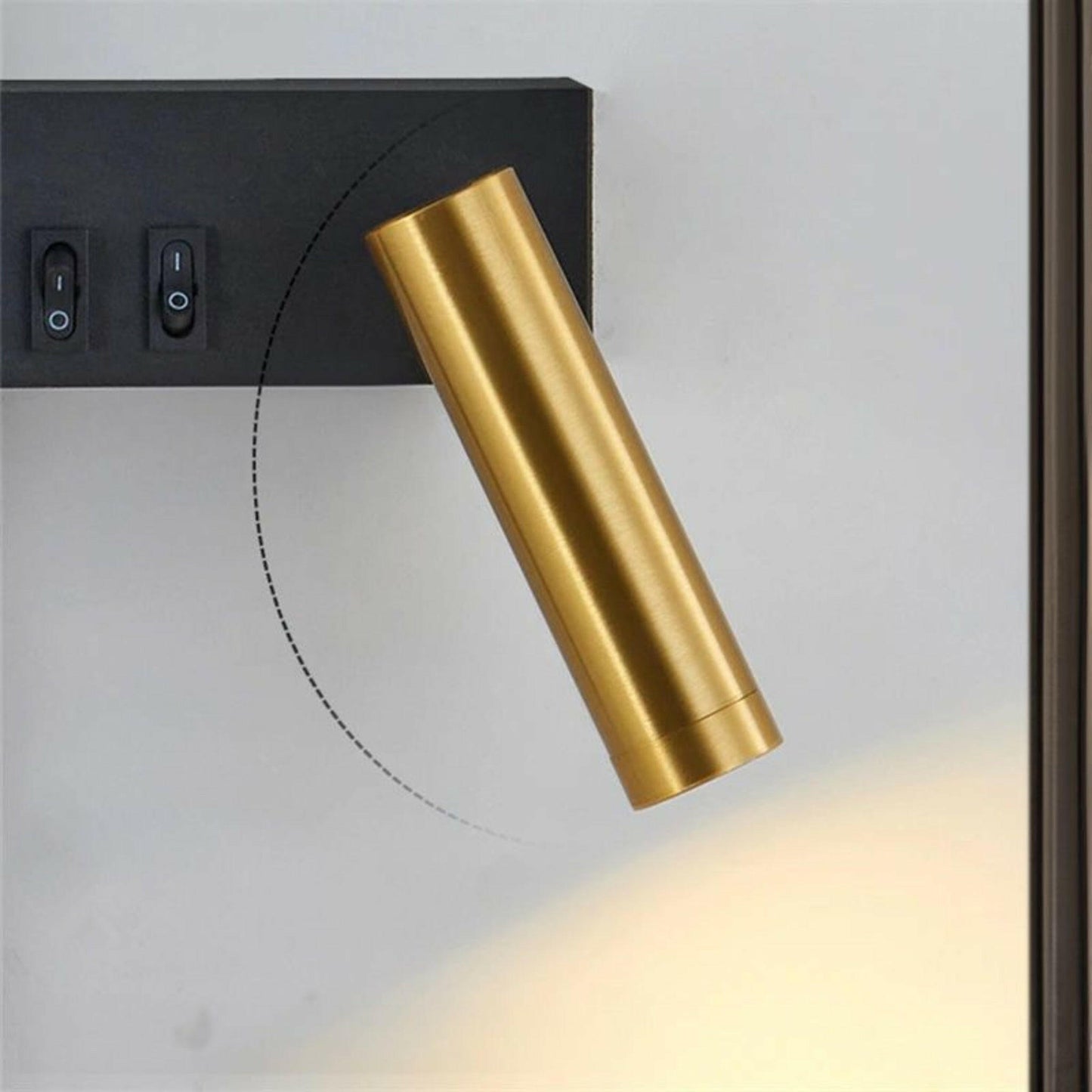 Gold cylindrical wall light fixture on a white wall with black electrical box.