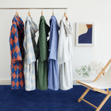 Hanging clothing items on a rack against a white wall with a chair and abstract art in the background.