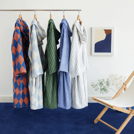 Hanging clothing items on a rack against a white wall with a chair and abstract art in the background.