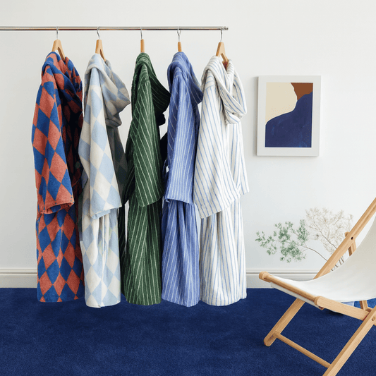Hanging clothing items on a rack against a white wall with a chair and abstract art in the background.