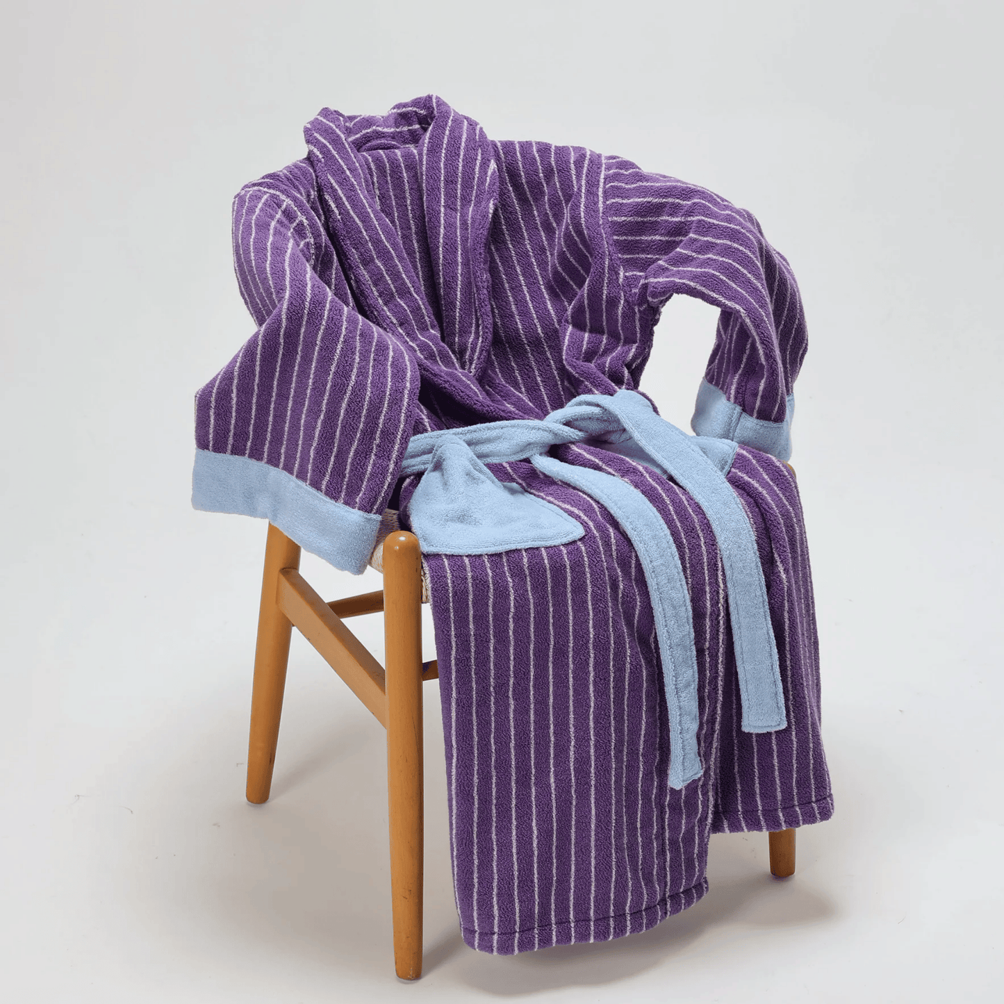 Purple striped robe draped over a wooden chair with a blue towel underneath on a white background
