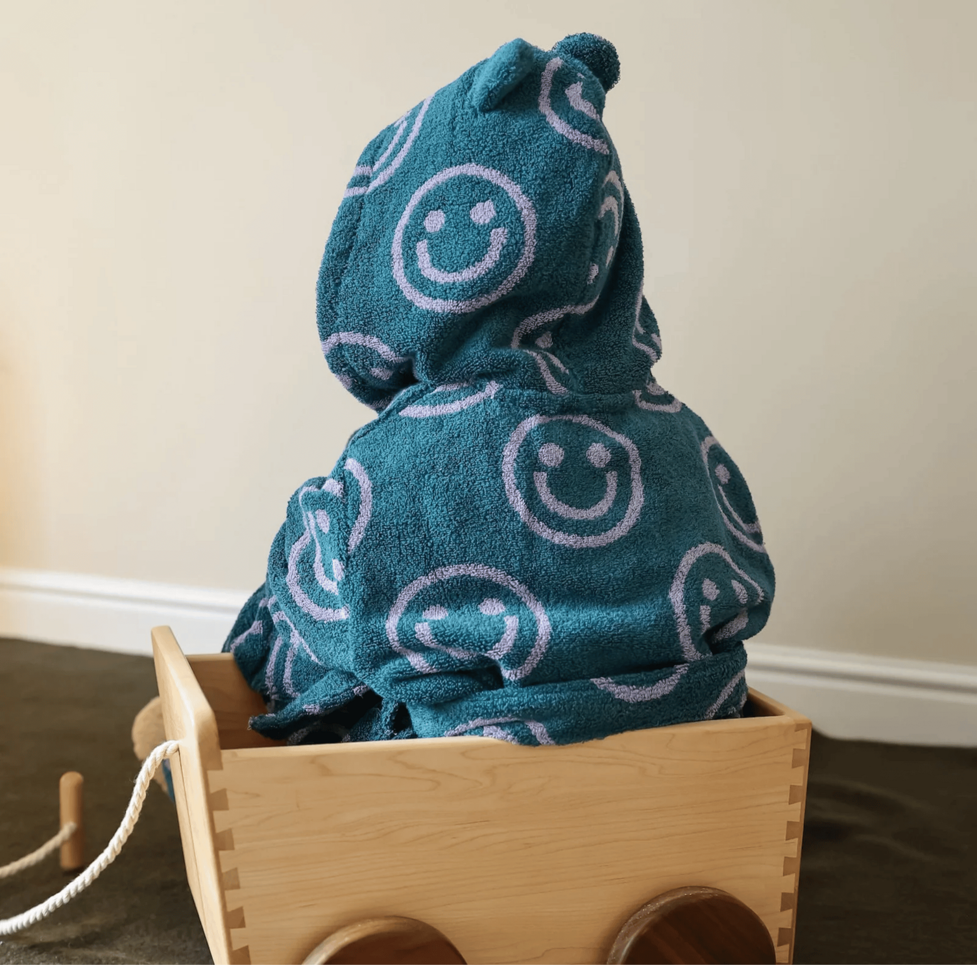 Blue hooded towel with smiley face pattern on a wooden toy cart.