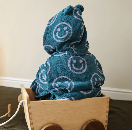 Blue hooded towel with smiley face pattern on a wooden toy cart.