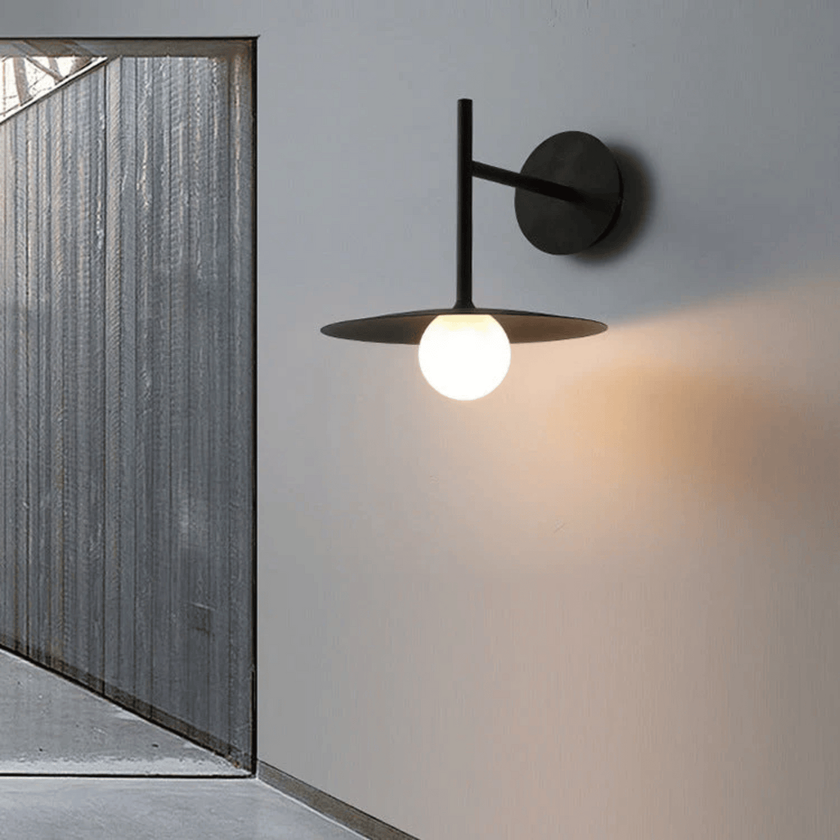 Modern wall-mounted light fixture on a gray wall with a glass door in the background.